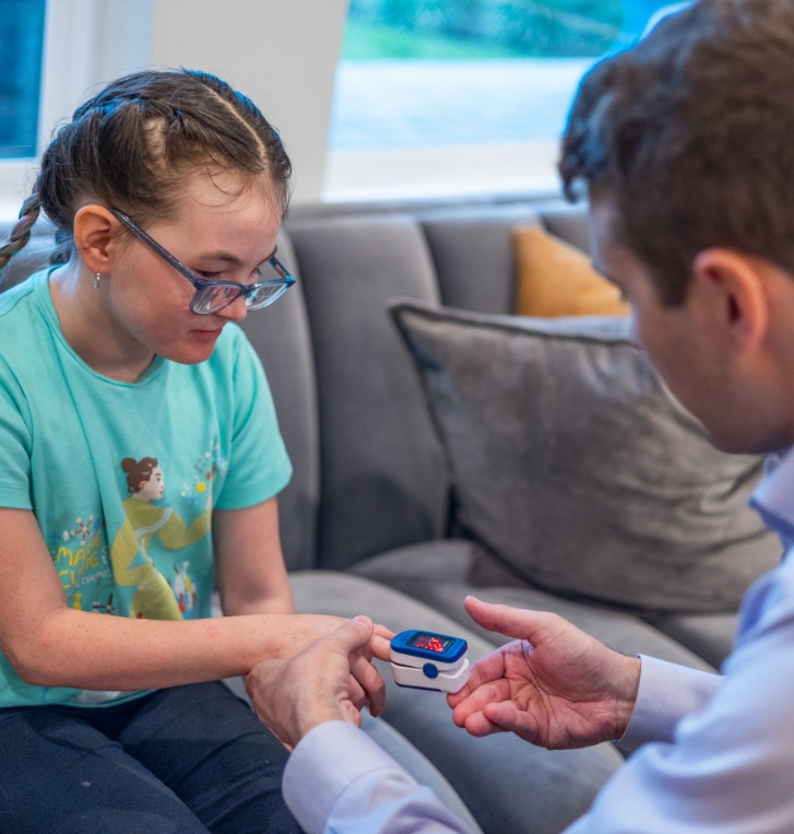 Doctor Weiss using a pulse oximeter on a girl with glasses and braids