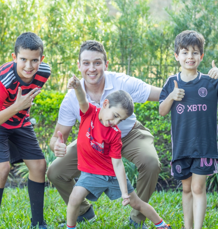 Orlando pediatrician smiling and giving thumbs up with three kids outdoors in soccer uniforms