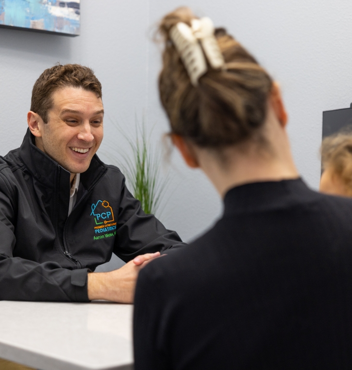 Orlando pediatrician smiling at a patient in their mothers lap across desk