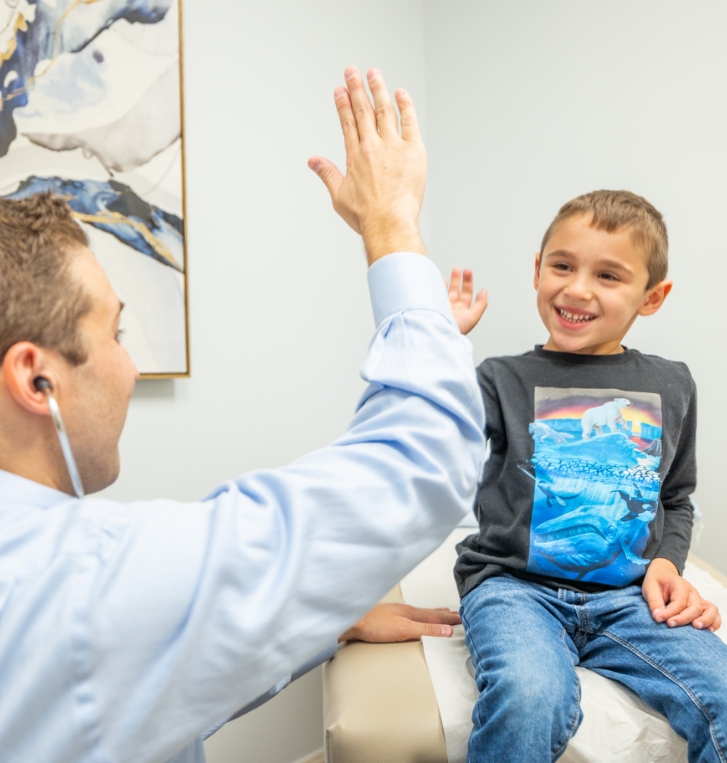Doctor Weiss giving a high five to a young boy in pediatrician office