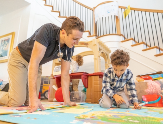 Doctor Weiss watching a child draw on a map of the world on the floor